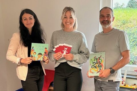 Die Kinderschutzfachkräfte Jennifer Laupp (link) und Kjara Allion übergeben Thomas Toth (Leiter Kita Villa Regenbogen) die Bücher, mit denen zukünftig in den Kitas gearbeitet werden soll.