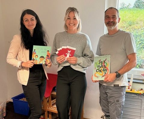 Die Kinderschutzfachkräfte Jennifer Laupp (link) und Kjara Allion übergeben Thomas Toth (Leiter Kita Villa Regenbogen) die Bücher, mit denen zukünftig in den Kitas gearbeitet werden soll.